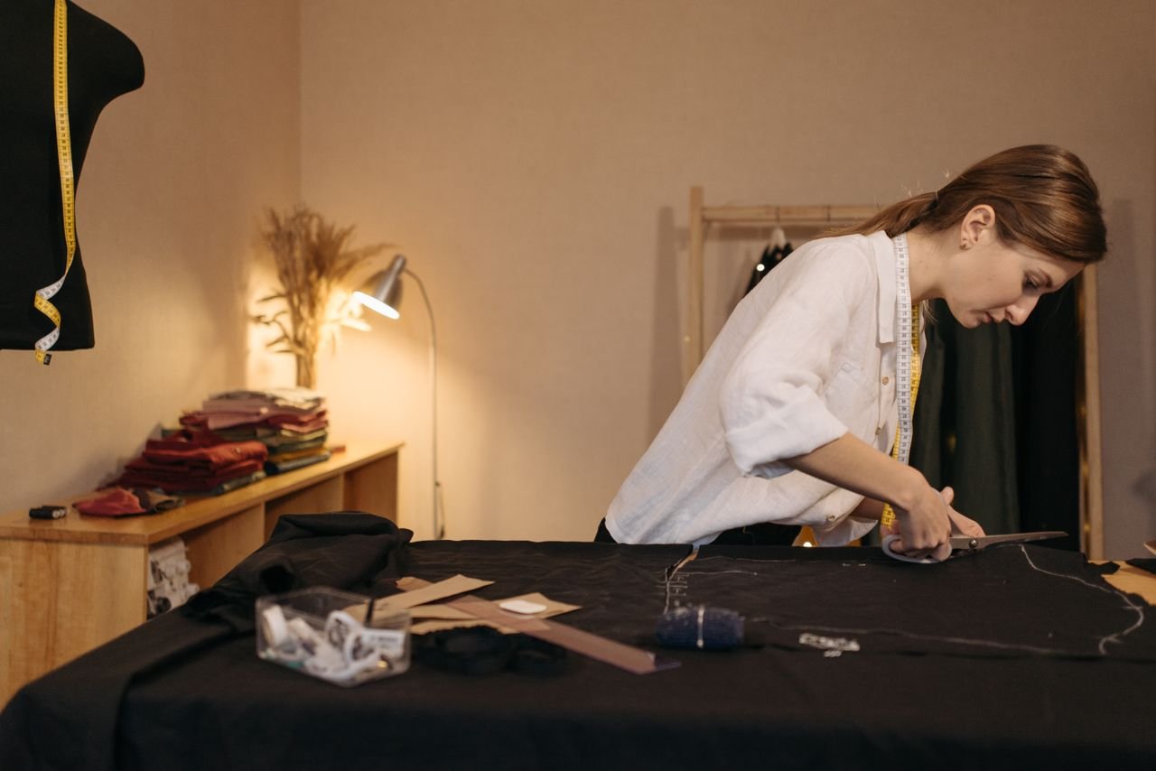 Behind the Seams: Meet the Tiny Team Creating Big Styles in Ohio Fashion designer cutting fabric in a workshop, focusing on garment creation.