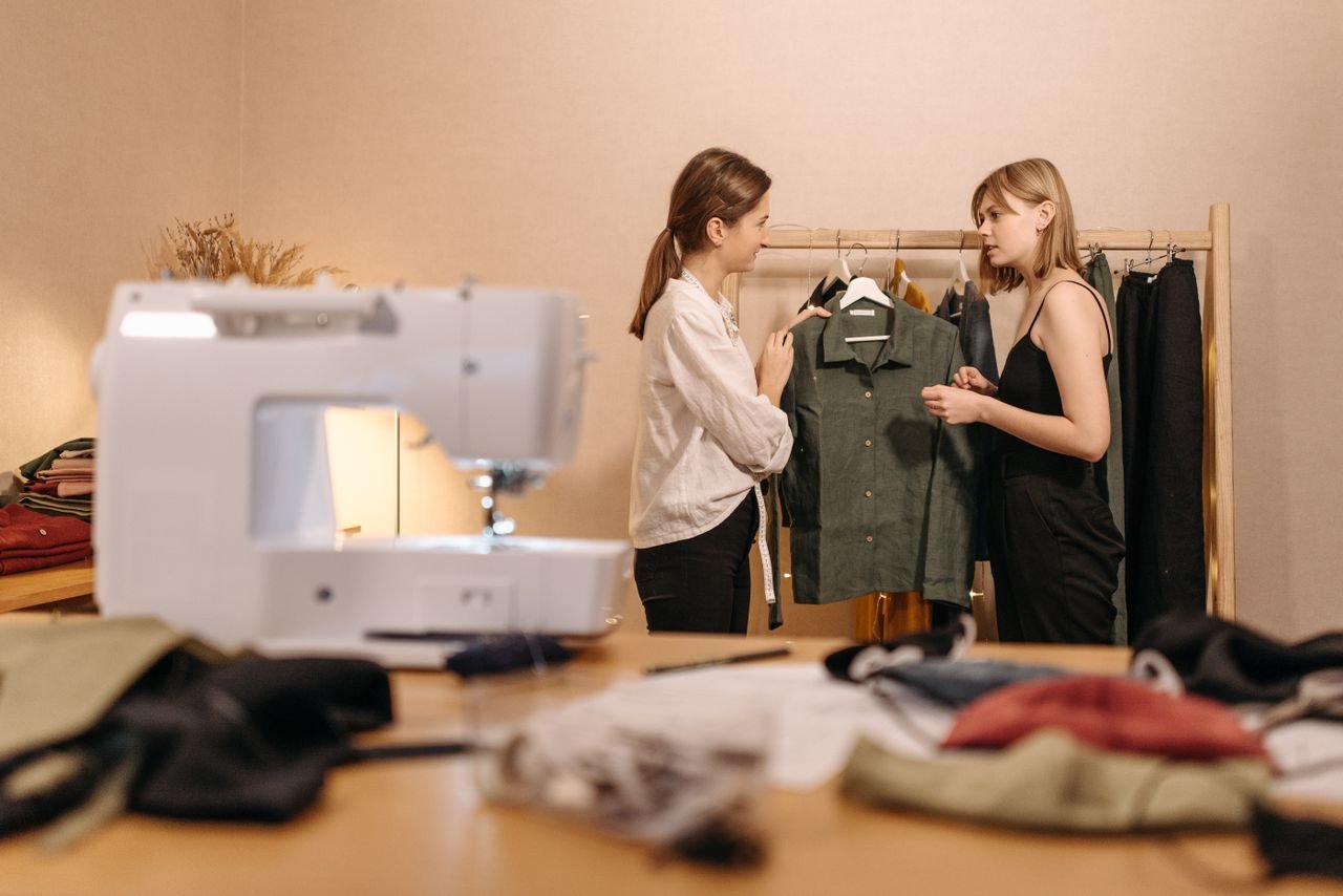How to Build a Capsule Wardrobe with Unique Statement Pieces Two women in a fashion studio discussing clothing designs with a sewing machine in the foreground.